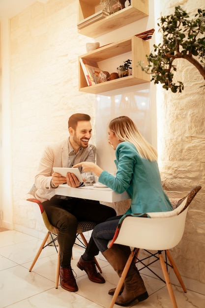 カフェに座ってデジタルタブレットに取り組んでいる2人の美しい若い笑顔のビジネスマン。セレクティブフォーカス。