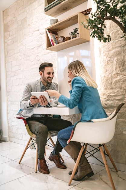 Two beautiful young smiling people sitting at cafe and working on digital tablet.