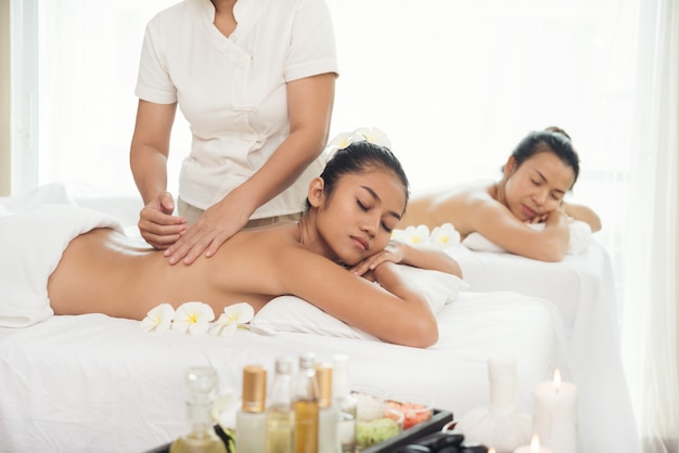 Two Beautiful young woman getting spa massage salon and white flower on her head.