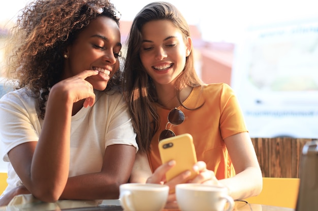 Two beautiful young woman sitting at cafe drinking coffee and looking at mobile phone.