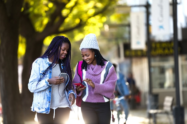 Two beautiful young woman using mobile phone in the street.