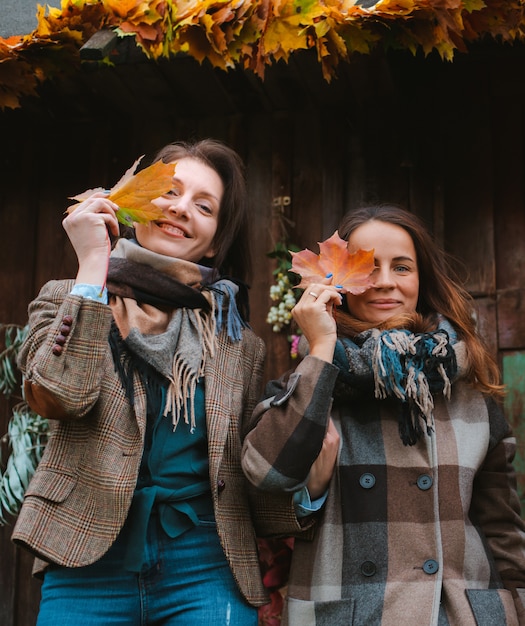 Foto due belle giovani donne, che coprono i loro volti con autunno giallo sullo sfondo di legno.