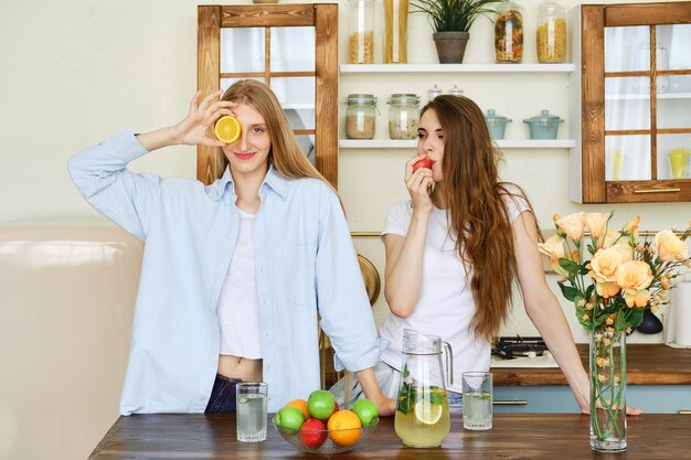 Two beautiful young women eat fruits in the kitchen