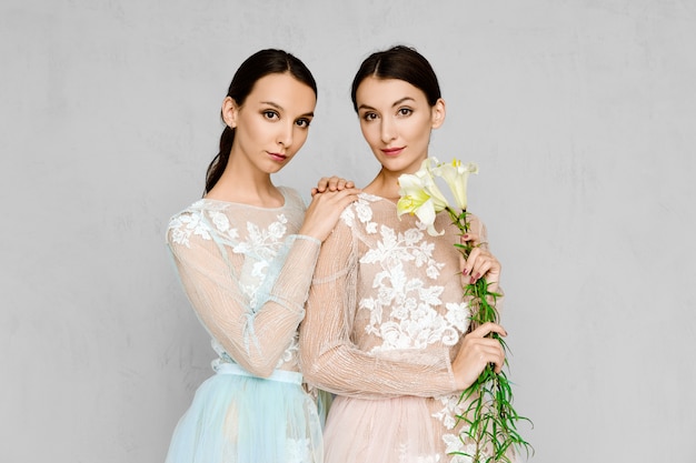 Две красивые молодые женщины в прозрачных платьях из тюля с кружевом позируют одинаково