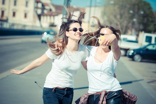 Photo two beautiful young women using smart phone selfie