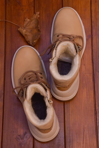 Due scarpe autunnali beige con lacci stanno su uno sfondo marrone in legno con una foglia d'acero secca.