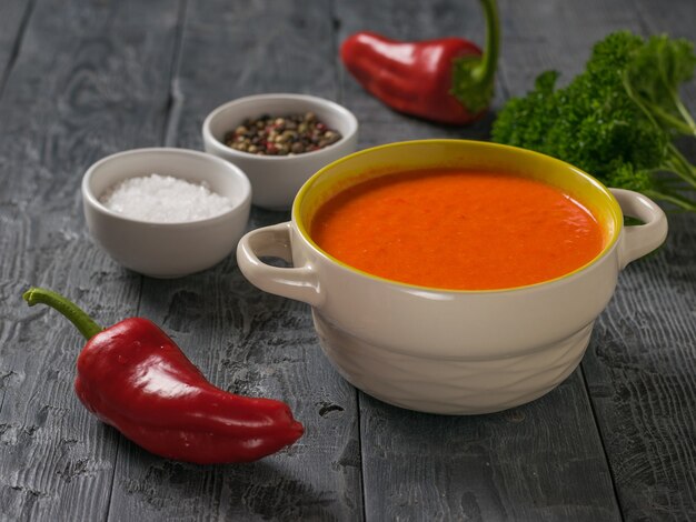 Two bell peppers with cream soup and seasonings on a wooden table. Soup of the vegetarian diet.