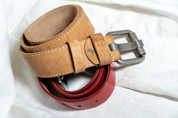 Two belts made of thick genuine leather on a white background made of linen fabric Production of handmade belts from natural environmentally friendly materials