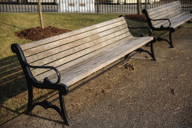 Two benches are sitting on a sidewalk, one has a black armrest.