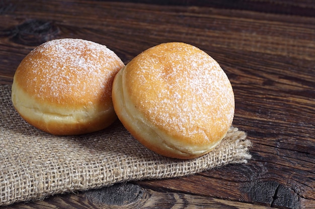 Two berliner donuts with powdered sugar on wooden table