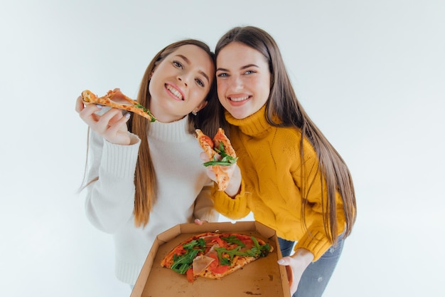 Two best friends eating appetizing pizza. Girls smiling, looking at camera and posing.