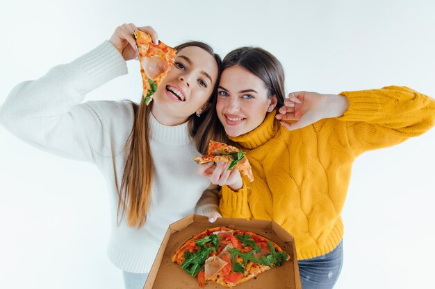 Two best friends eating appetizing pizza. girls smiling,\
looking at camera and posing.