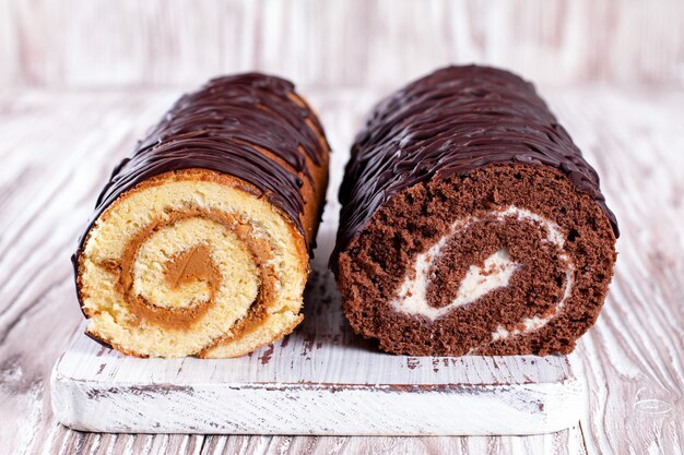 Two biscuit rolls. Chocolate and white cream sponge roll on the wooden cutting board