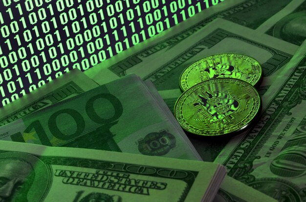 Two bitcoins lies on a pile of dollar bills on the background of a monitor