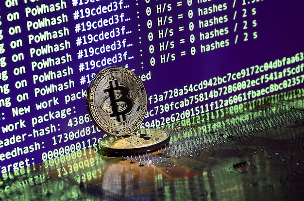 two bitcoins lies on a videocard surface with background of screen display of cryptocurrency mining by using the gpus