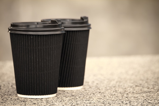 Two black disposable cups of coffee with lids are standing on the stone parapet