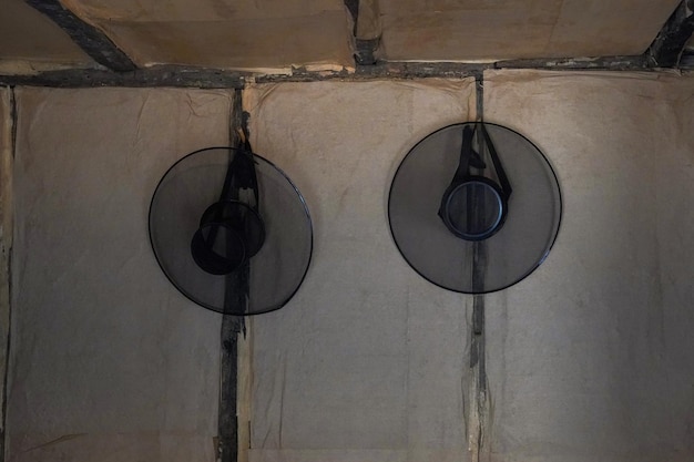 Two black fans hang on a wall, one of which is covered in black plastic.