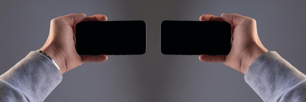 Two black modern rectangular smartphones in male hands on a gray isolated background screens of two