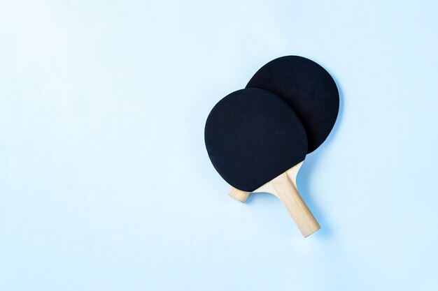 Two black ping pong paddles on light blue background