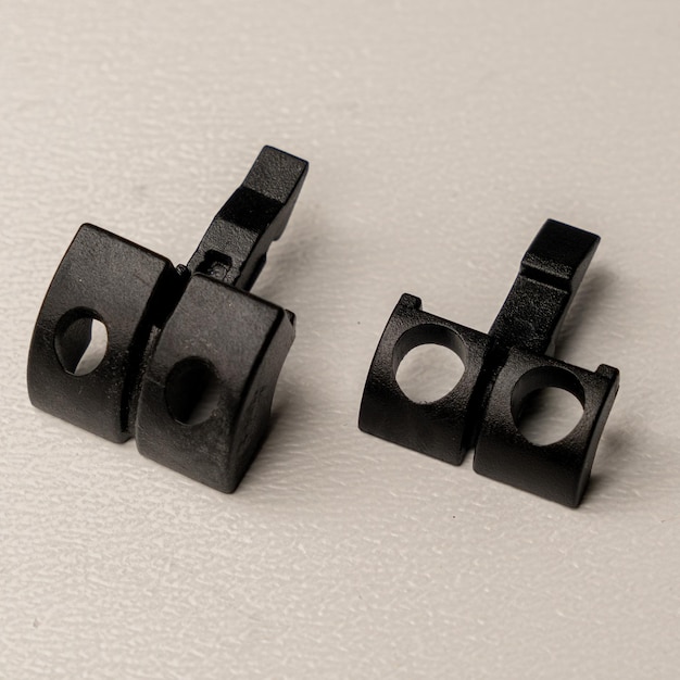 Two black plastic pieces with holes in them, one of which is labeled's.