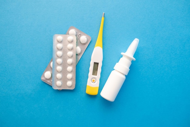 Two blisters with tablets a white bottle of nasal drops and a thermometer