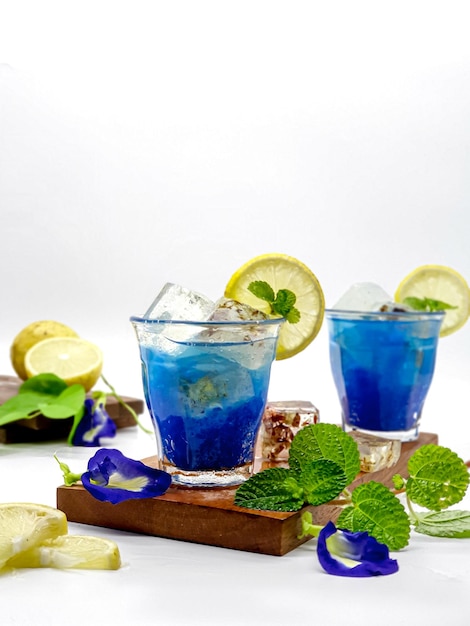 Two blue cocktails with lemons and mint leaves on a wooden board.