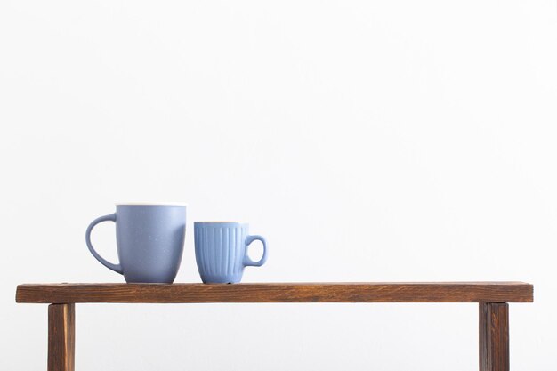 Photo two blue cups on wooden shelf on white background