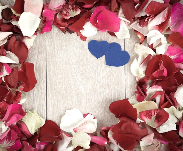 Two blue hearts in a frame of rose petals on a wooden background