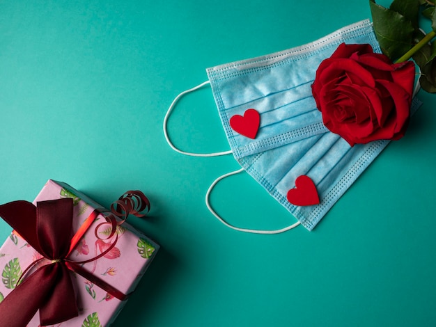 Two blue masks with two red hearts and a red rose on masks, and a pink gift on green