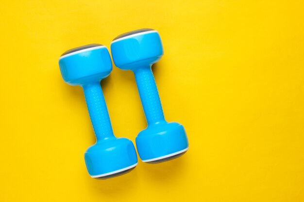 Two blue plastic dumbbells on yellow background