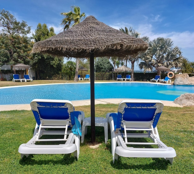 Two blue and white chairs are next to a pool with a blue umbrella.