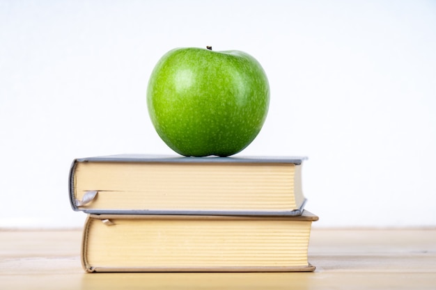 Two books and green apple on the wooden table, education