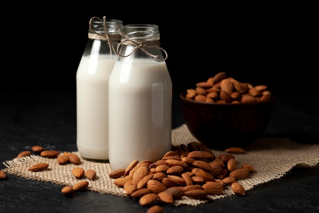 Two bottles of almond milk with nuts on a dark black table vegetarian milk without sugar and lactose