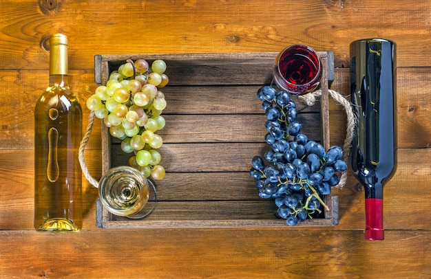 木製の背景にワインとブドウと2本のボトルとグラス。上面図、コピースペース。