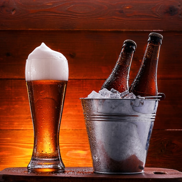 two bottles of beer in a bucket with ice and a glass of beer with lush foam