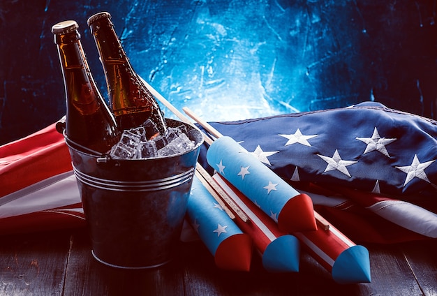 Due bottiglie di birra in un secchiello del ghiaccio con la bandiera americana che giace nelle vicinanze e razzi per fuochi d'artificio. concetto di celebrazione del giorno dell'indipendenza