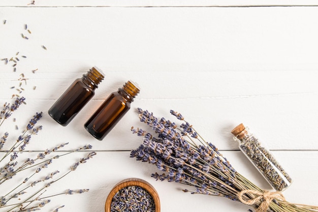 Due bottiglie di vetro scuro con olio essenziale di lavanda un bouquet di lavanda secca e semi su un tavolo di villaggio bianco visualizza una copia dello spazio