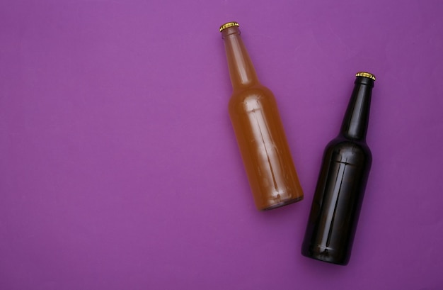 Two bottles of dark and light beer on a purple background. Top view. Copy space