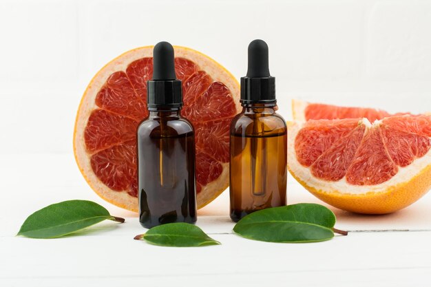 Two bottles of droppers with cosmetic grapefruit oil or facial serum against the background of fresh grapefruit fruit. a natural concept of self-care.