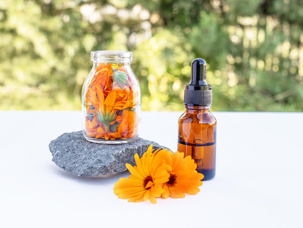 Foto due bottiglie di olio essenziale e fiori di calendula per la cura della pelle delle donne su sfondo naturale podio in pietra vista frontale