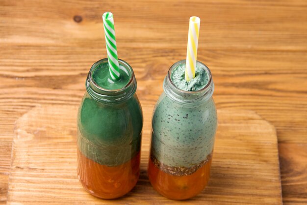 Two bottles of spirulina smoothie yogurt and orange jam on a wooden background