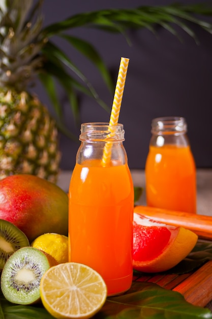 Two bottles of tropical exotic multifruit juice under a palm leaves with fruits on the background.