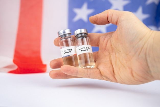 手にcovid-19ワクチンが入った2本のボトル。米国旗