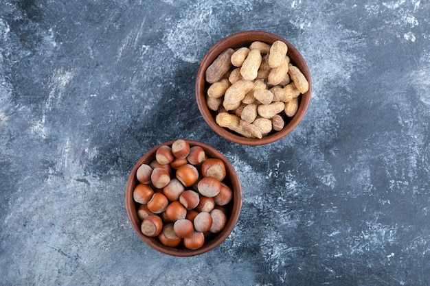 Two bowls of organic shelled peanuts and hazelnuts on marble.