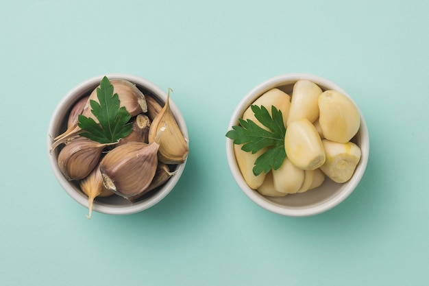 Two bowls of peeled and unpeeled garlic and parsley leaves on a blue surface. A popular spice for the kitchen.