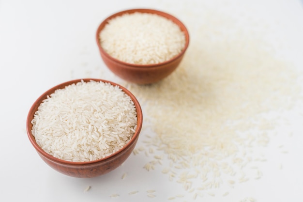 Photo two bowls of raw rice with scattered rice over white surface