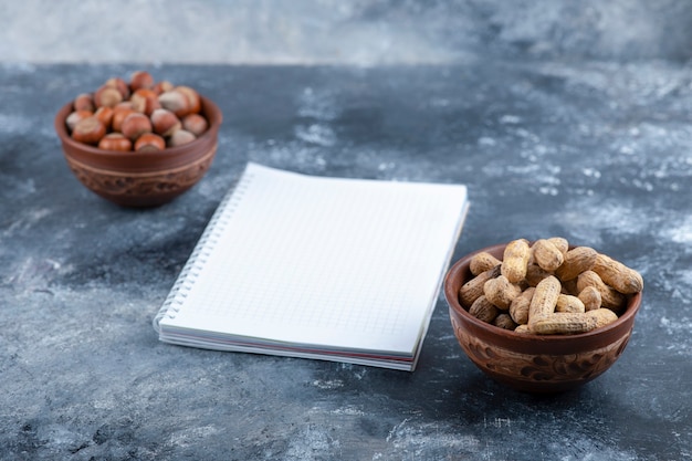 Two bowls of shelled hazelnuts and peanuts with empty page.