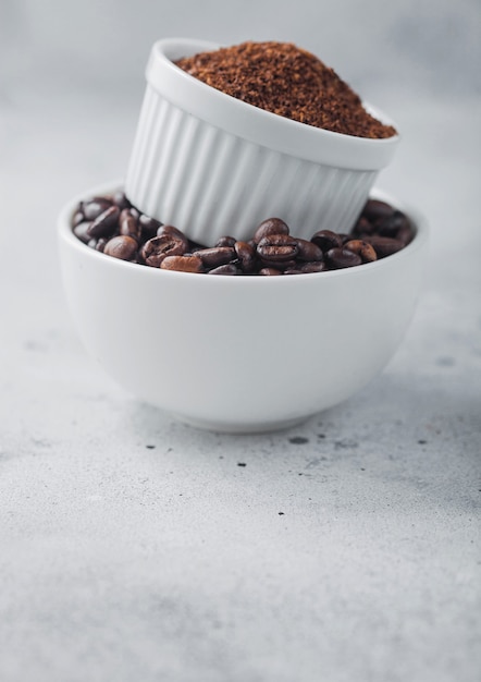 Two bowls on top of each other with fresh raw coffee beans and powder on light table background.