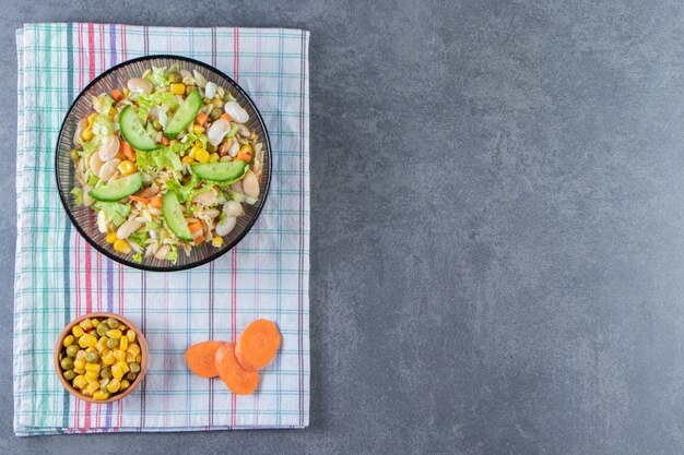 Two bowls of vegetable salad and sliced carrot on a tea towel, on the marble surface