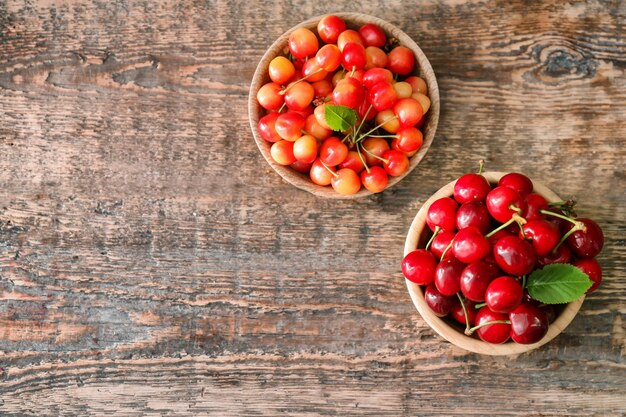 Two bowls with fresh ripe cherries on wooden background